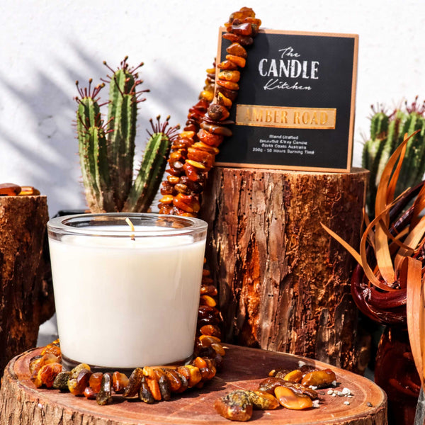 Amber Road Soy Candle The Candle kitchen, The Candle Kitchen beautiful candle surrounded with amber stones on a wooden log, surrounded by cactus and dried leaves.