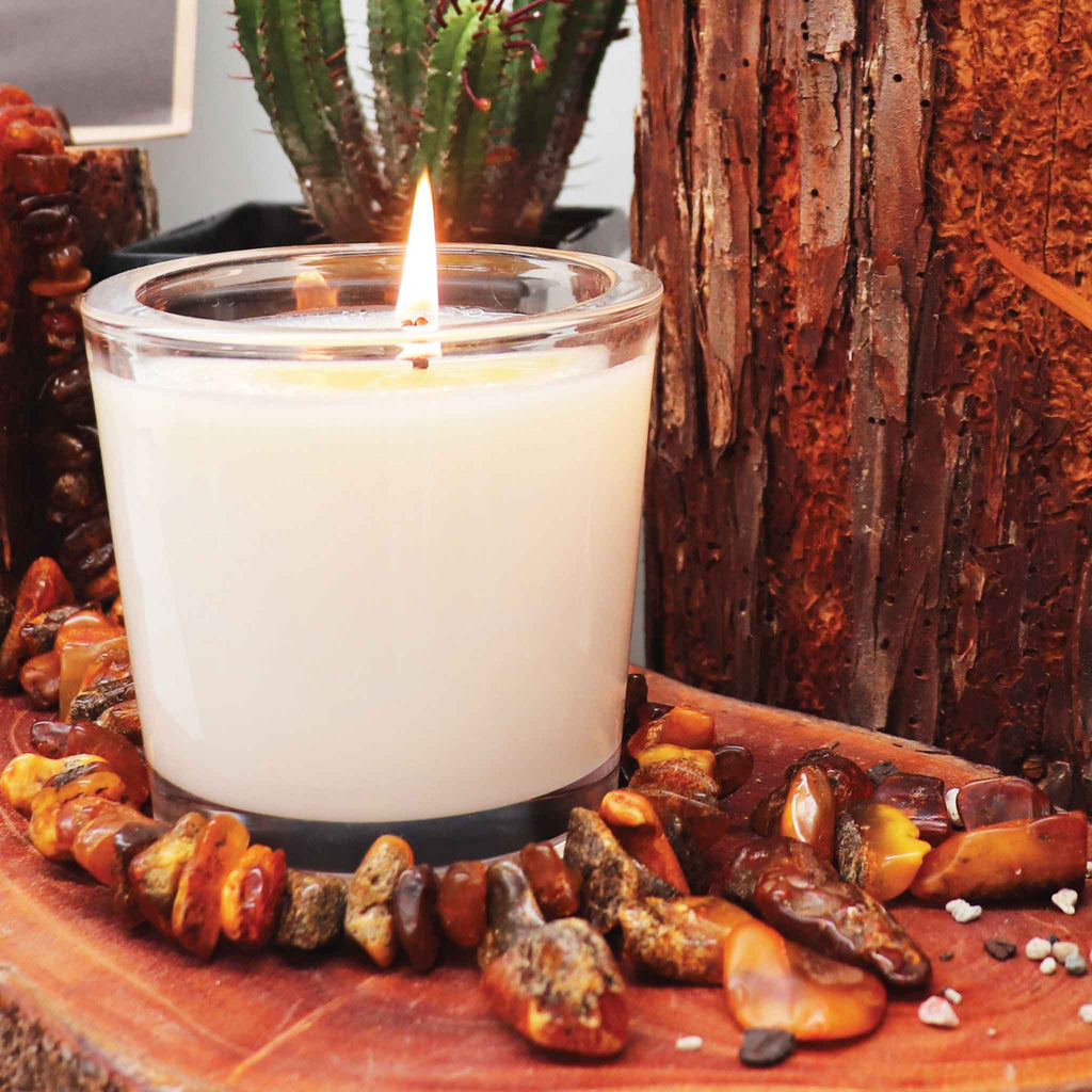 A Creamy white Candle from the Candle Kitchen with a flickering flame, chunky amber stones surrounded by rich red wood.