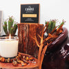 A Creamy white Candle from the Candle Kitchen with a flickering flame, chunky amber stones surrounded by rich red wood.