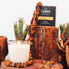 The Candle Kitchen beautiful candle surrounded with amber stones on a wooden log, surrounded by cactus and dried leaves.