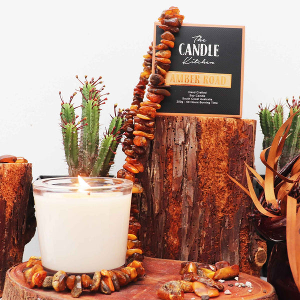 The Candle Kitchen beautiful candle surrounded with amber stones on a wooden log, surrounded by cactus and dried leaves.