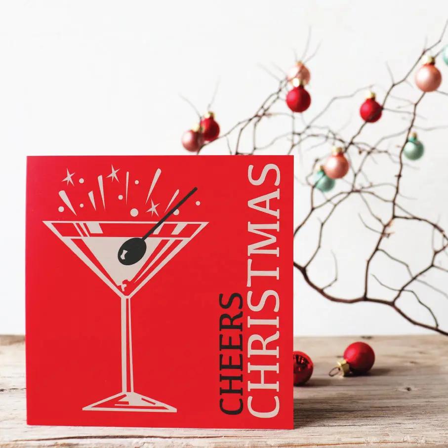 A Christmas card with a graphic of Santa Claus and the text 'HAVE A HOLY JOLLY CHRISTMAS' in red and white on a black background, displayed on a wooden surface with holiday decorations in the background.