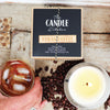 The Candle Kitchen Coffee Creme Candle with coffee beans, a flickering candle flame. on a wooden surface.