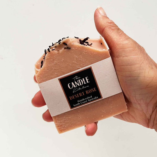 Hand holding a bar of soap with 'The Candie Kitchen' label on a light background