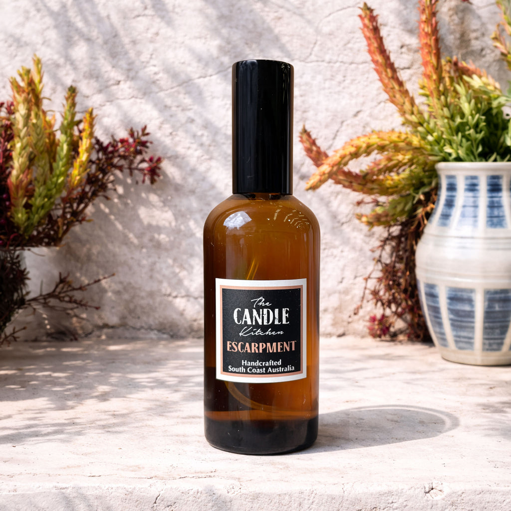 Bottle of 'The Candle Kitchen Escarpment' on a textured surface with plants in the background