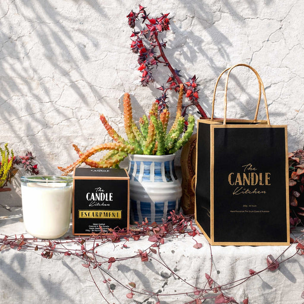 Escarpment Soy Candle and packaging from 'The Candle Kitchen' with decorative plants on a textured surface.