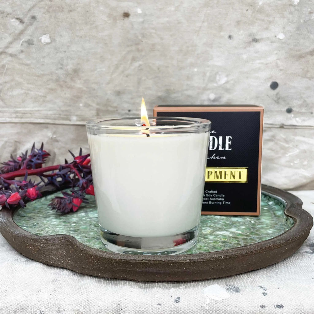 A close up of a candle made by the Candle Kitchen, on a hand made ceramic dish.