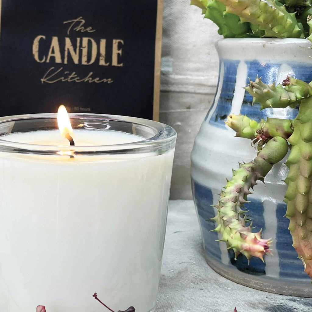 A close up of a candle made by the Candle Kitchen, with a succulent plant on the right side.