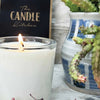 A close up of a candle made by the Candle Kitchen, with a succulent plant on the right side.