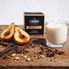 Candle with 'The Candle Kitchen' packaging, pears, and spices on a wooden surface.