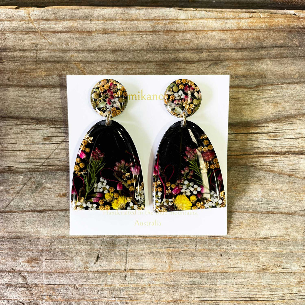 Pair of floral earrings on a white card with 'mikano' branding, placed on a wooden surface.