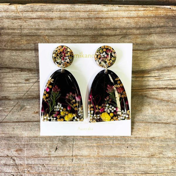Pair of floral earrings on a white card with 'mikano' branding, placed on a wooden surface.