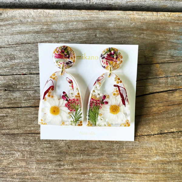 Floral earrings on a card with 'mikano' branding, placed on a wooden surface.
