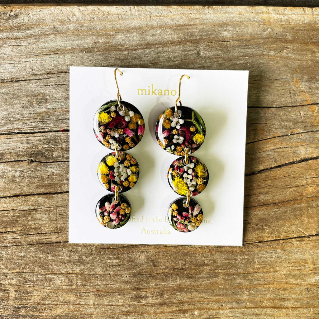 Floral earrings on a white card with 'mikano' branding, placed on a wooden surface.