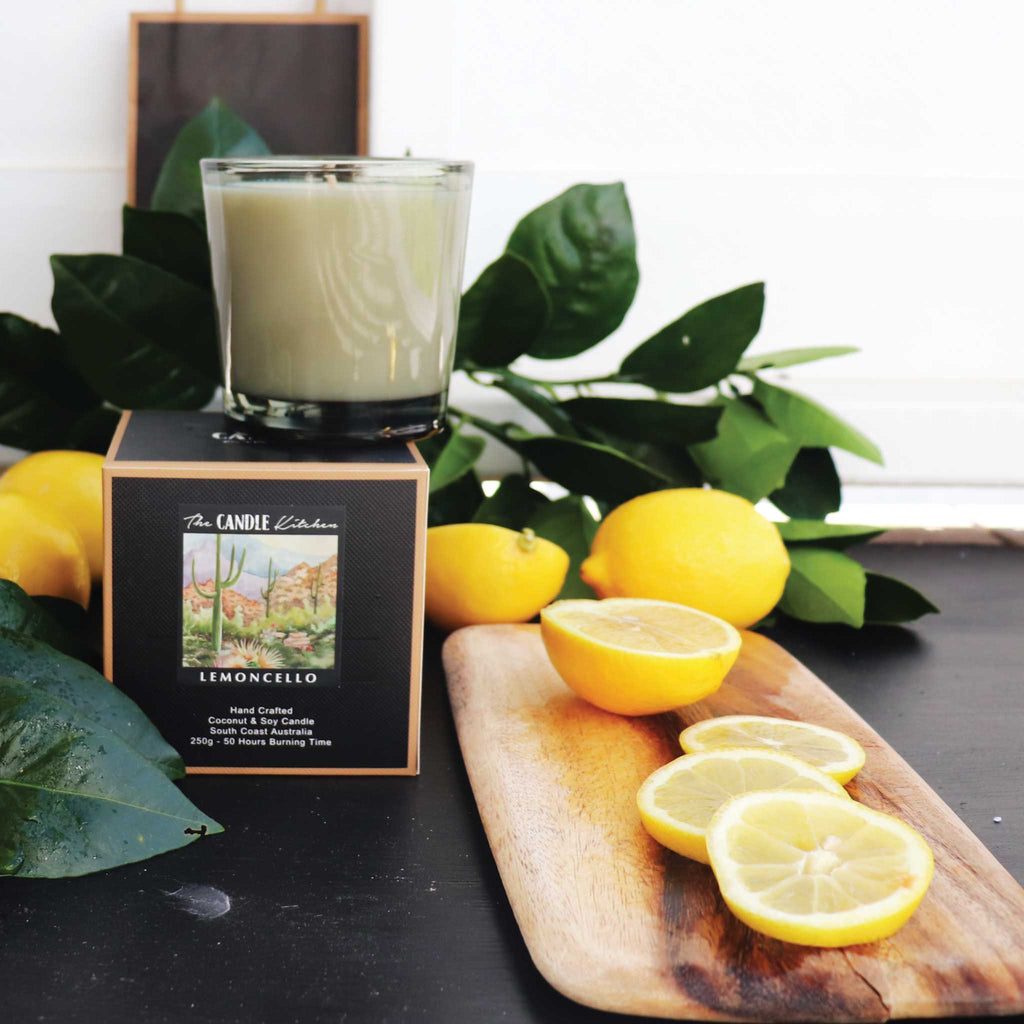 A shinny glass Candle with juicy lemon fruit on a wooden board with lemons and green leaves From the Candle Kitchen.