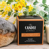 The Candle Kitchen packaging from 'The Candle Kitchen' with yellow wattle flowers and a convict brick in the background