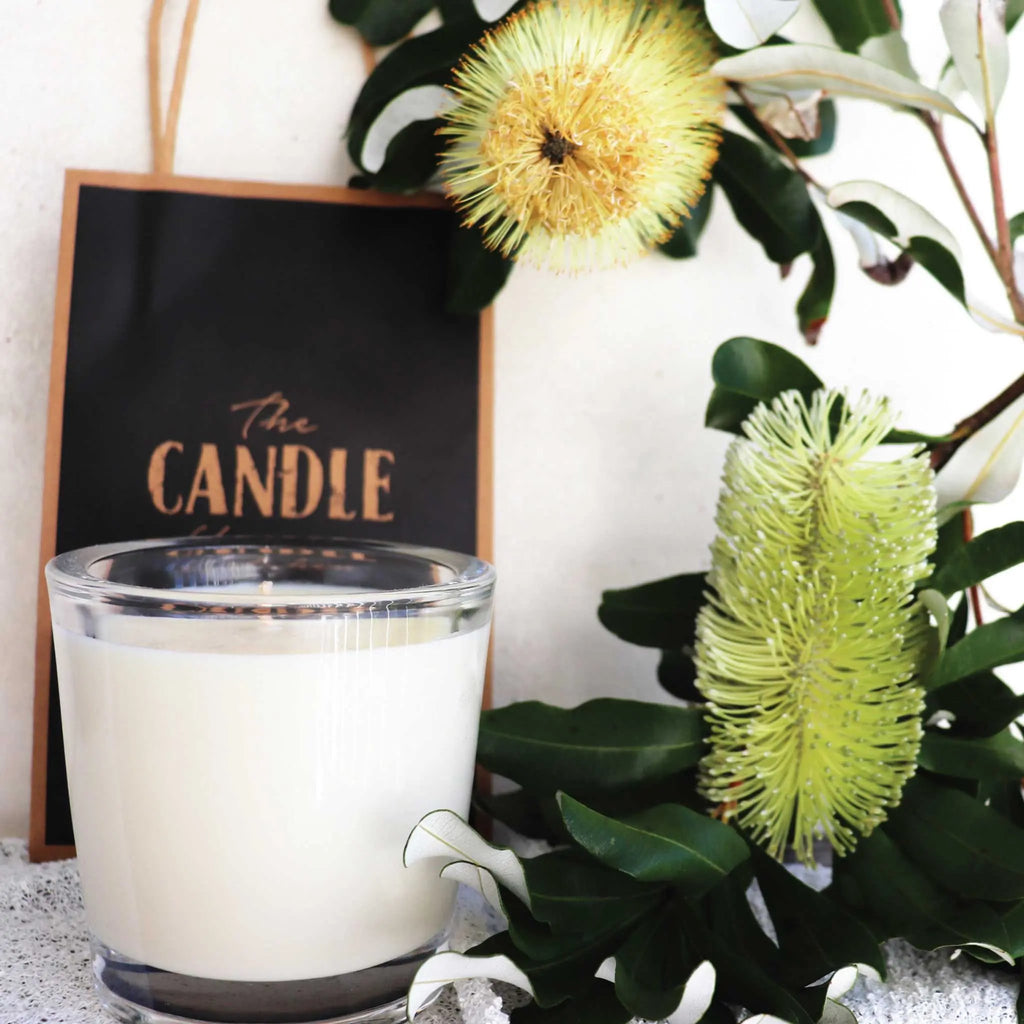 A close up of a creamy white candle from the South Coast of Australia with 2 yellow Banksia flower in the background.