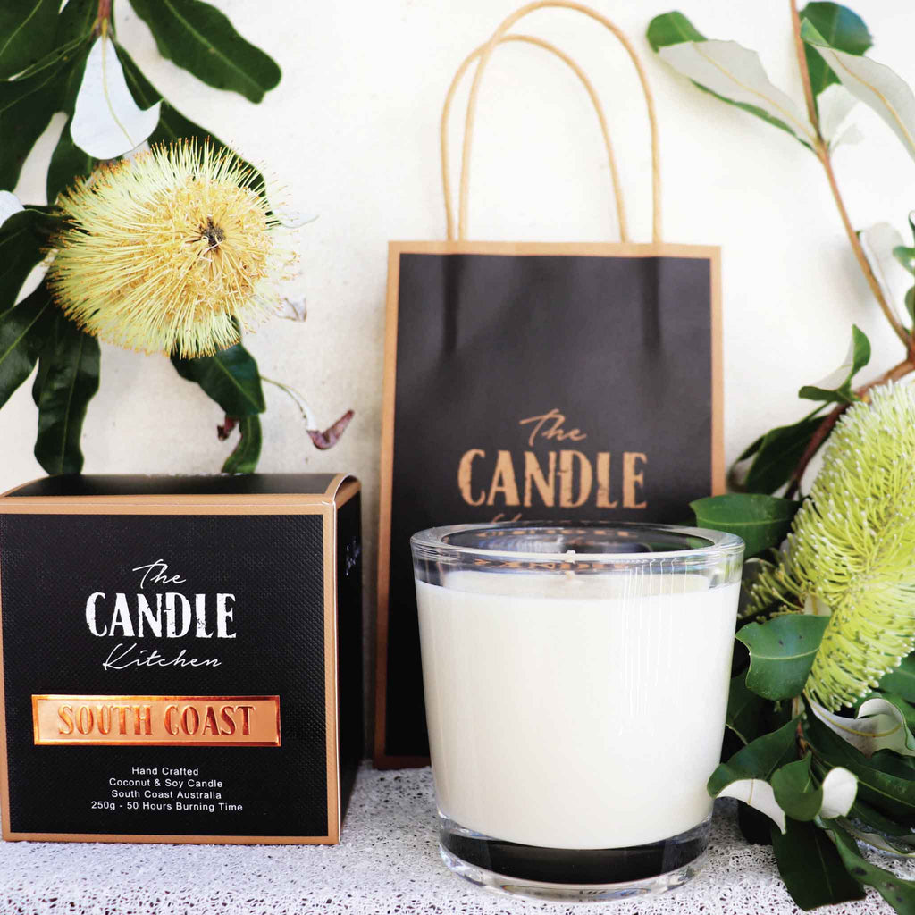 A close up of a creamy white candle from the Candle Kitchen on the South Coast of Australia with 2 yellow Banksia flower in the background.