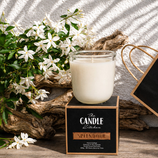 Splendour Soy Candle The Candle kitchen, Candle with packaging and flowers on a textured surface Candle in a glass jar with a decorative label on a wooden surface with flowers and driftwood.