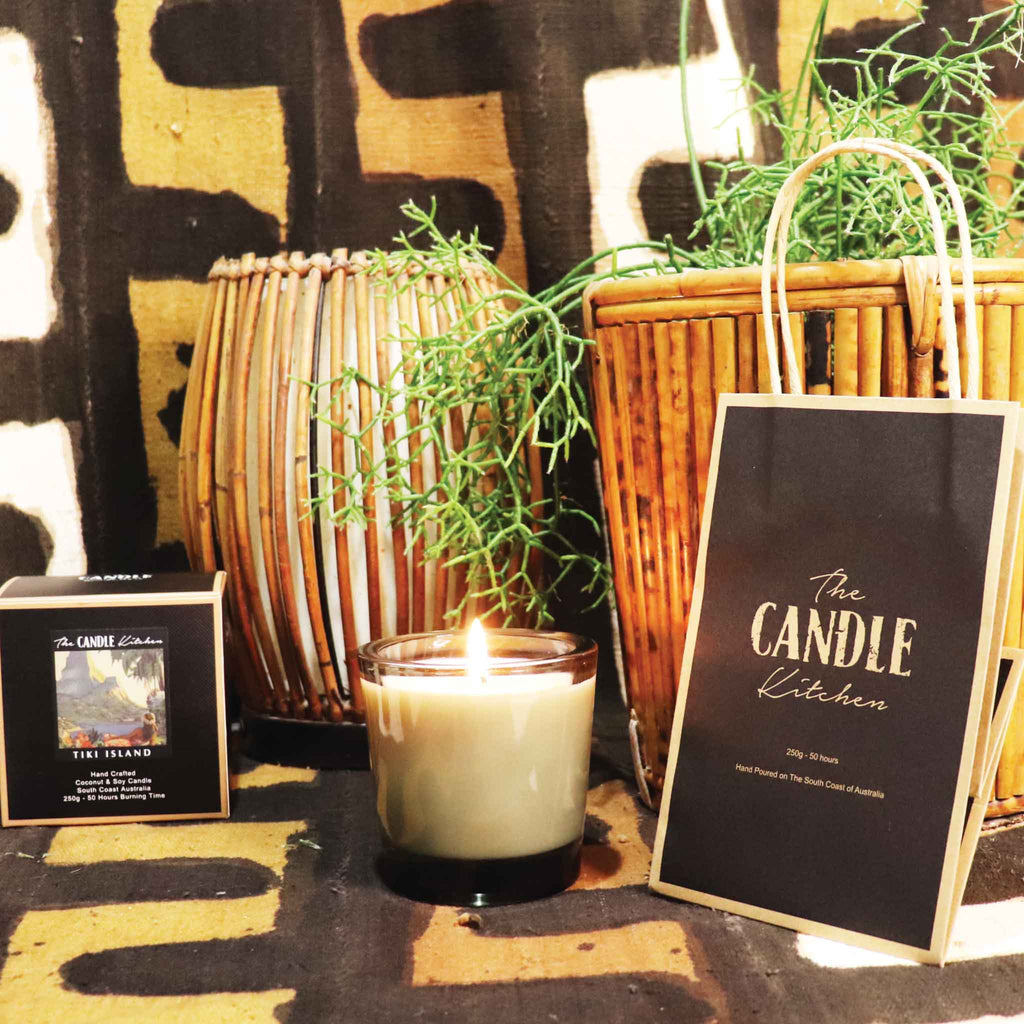 Candle with a bamboo retro table light , and a green cactus pot plant on the side.  'The Candle Kitchen' bag on a textured African designed rug.