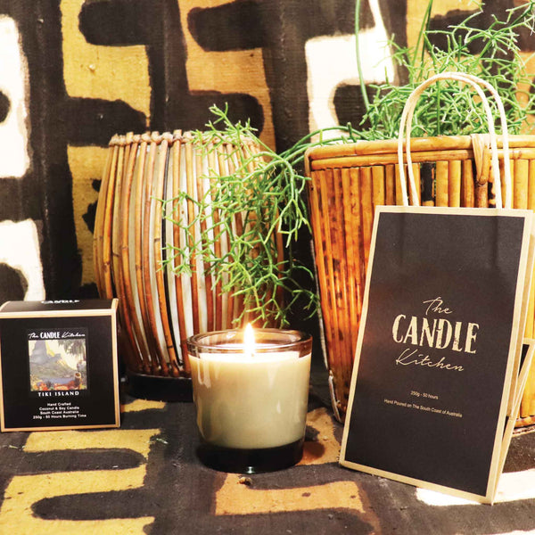 Candle with a bamboo retro table light , and a green cactus pot plant on the side.  'The Candle Kitchen' bag on a textured African designed rug.