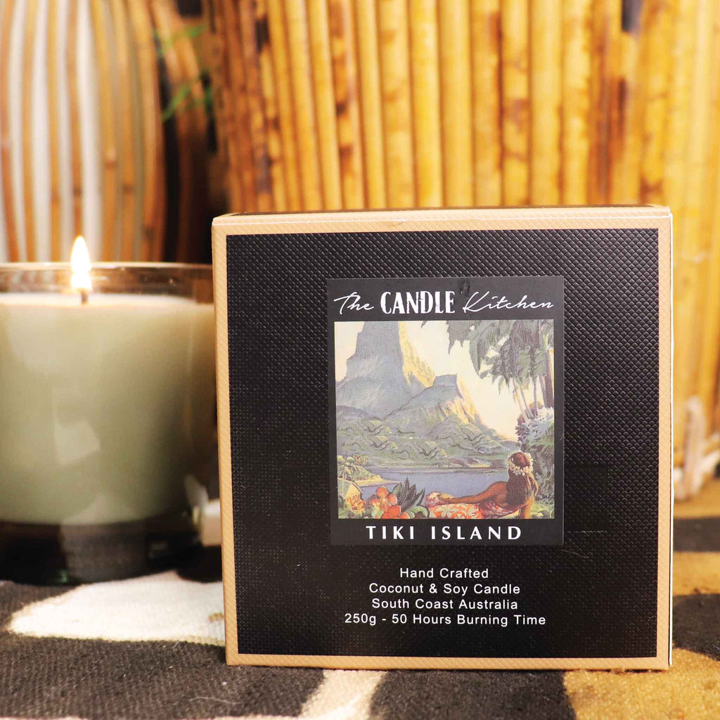 Candle Kitchen packaging with a retro Hawaiian girl label next to a lit candle against a bamboo background.