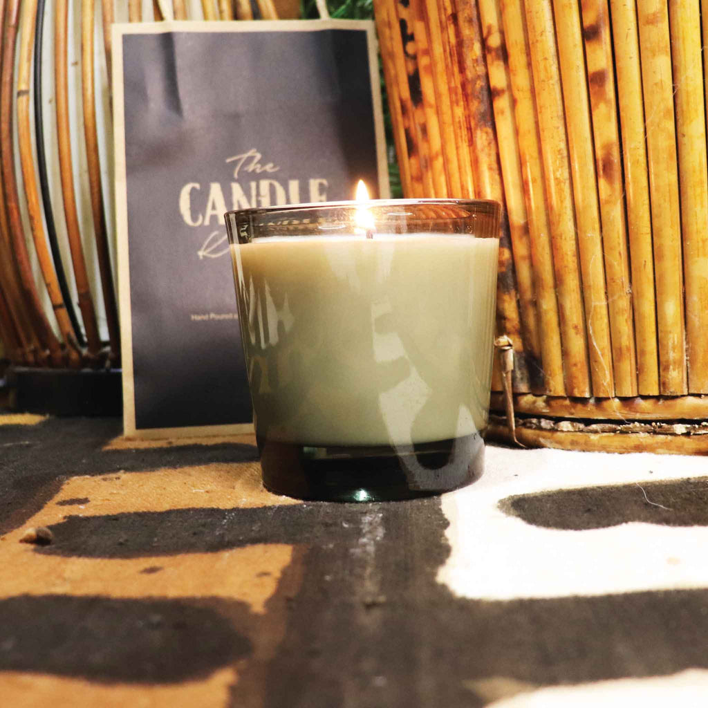 The Candle Kitchen in a glass holder with a bamboo background on an African designed fabric.