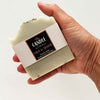 Hand holding a bar of soap with a visible label on a light background