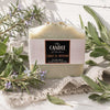 Sage and wood handmade soap surrounded by rosemary and sage on a linen tea towel