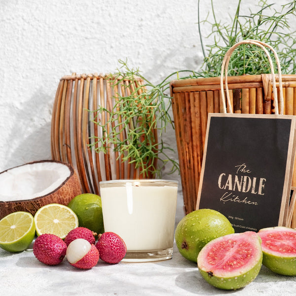 Tiki Island Soy Candle Kitchen , Candle with fruits and a basket on a white surface, featuring 'The Candle Kitchen' branding.